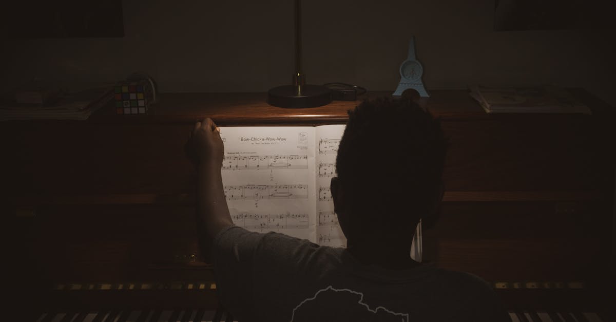 A musician practices piano in a dimly lit room, focusing intently on sheet music.