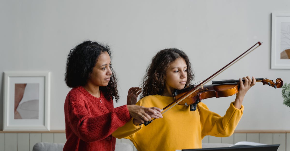 Mother assisting daughter with a violin lesson indoors, focusing on technique and posture.